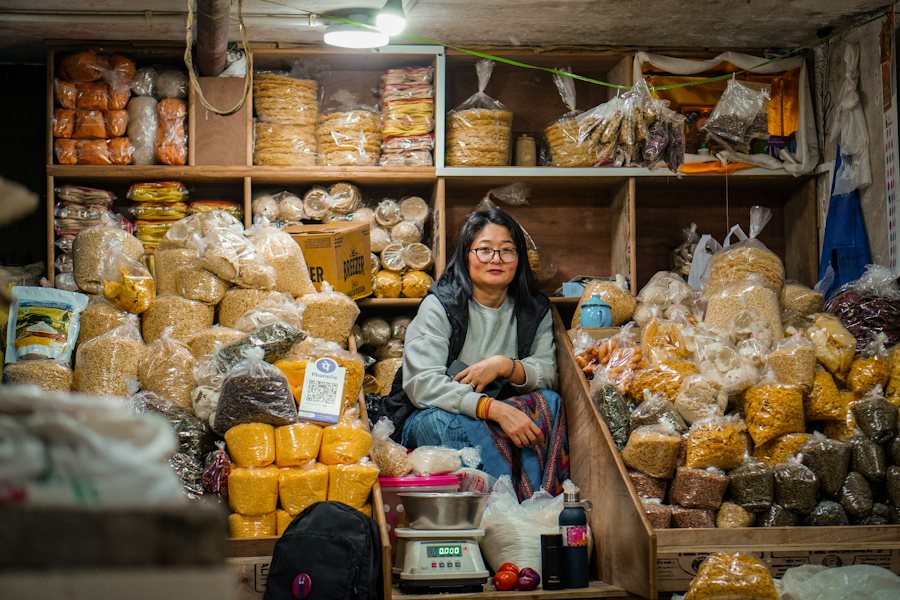 Mujer sentada en su tienda de abarrotes rodeada de mercancía