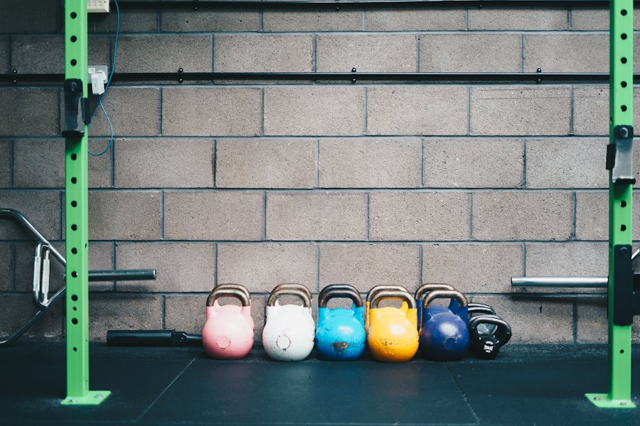 Kettlebells de colores frente a una pared de block